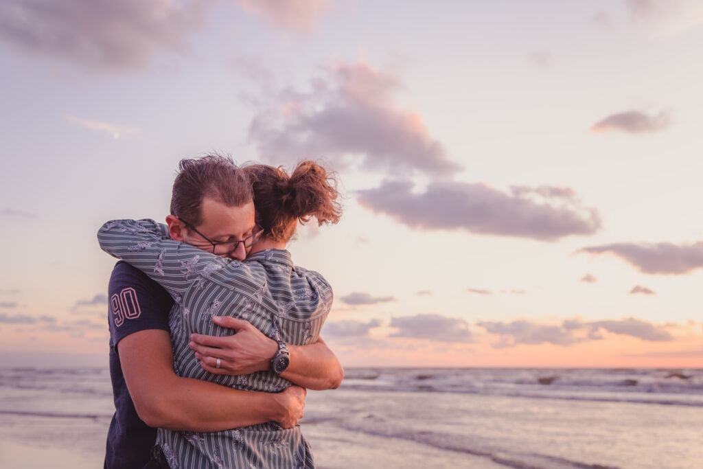 Intiem moment tussen een stel tijdens een fotoshoot aan het strand met de golven op de achtergrond